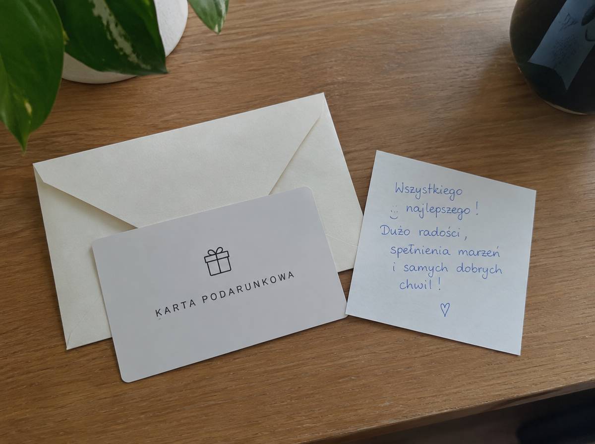 Karta podarunkowa w papierowej kopercie z odręczną kartką z życzeniami na biurku